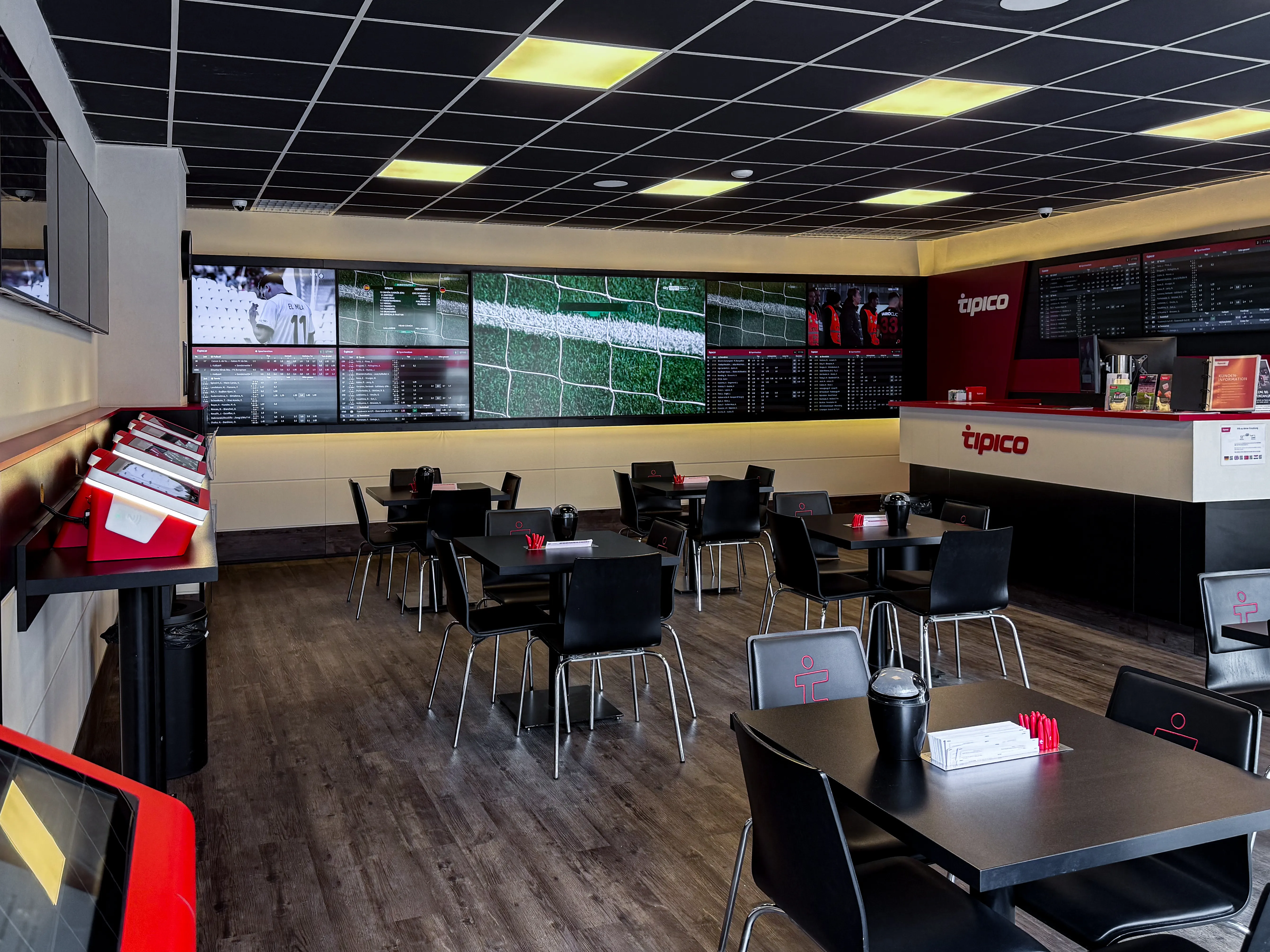 Innenraum mit großen Bildschirmen, Quotenboards, Theke und Sitzplätzen bei Tipico Wörrstadt